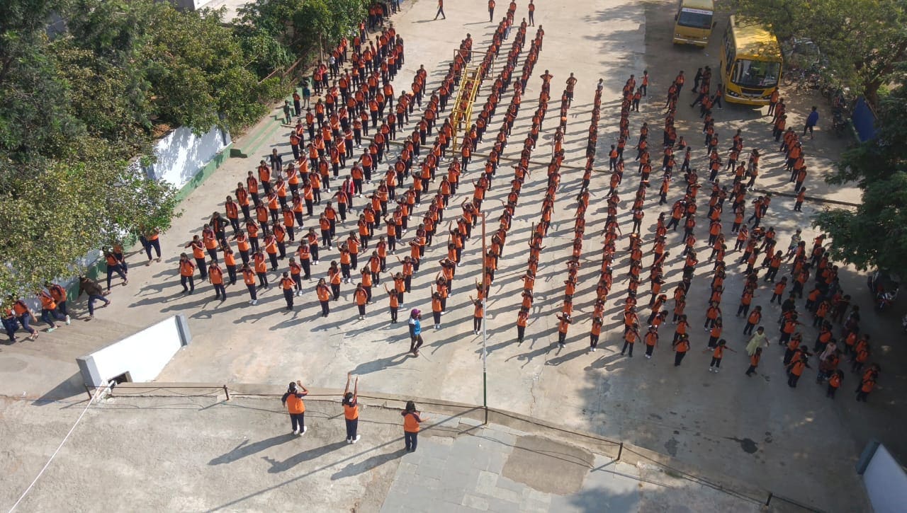 Aerial view of hundreds of students in uniform assembled in rows on the school grounds